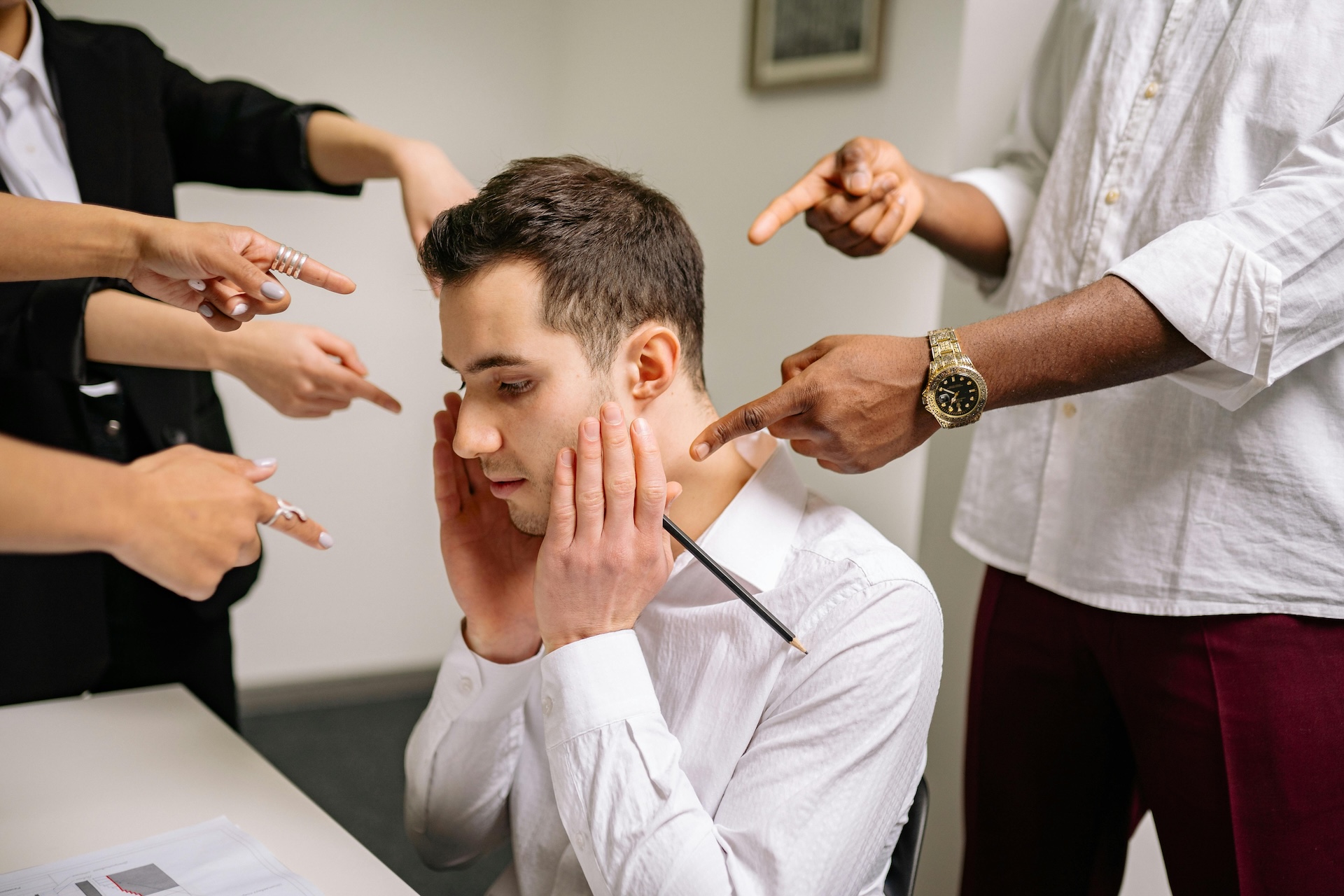 A man sitting down with his head resting in his hand while other people around are pointing at him