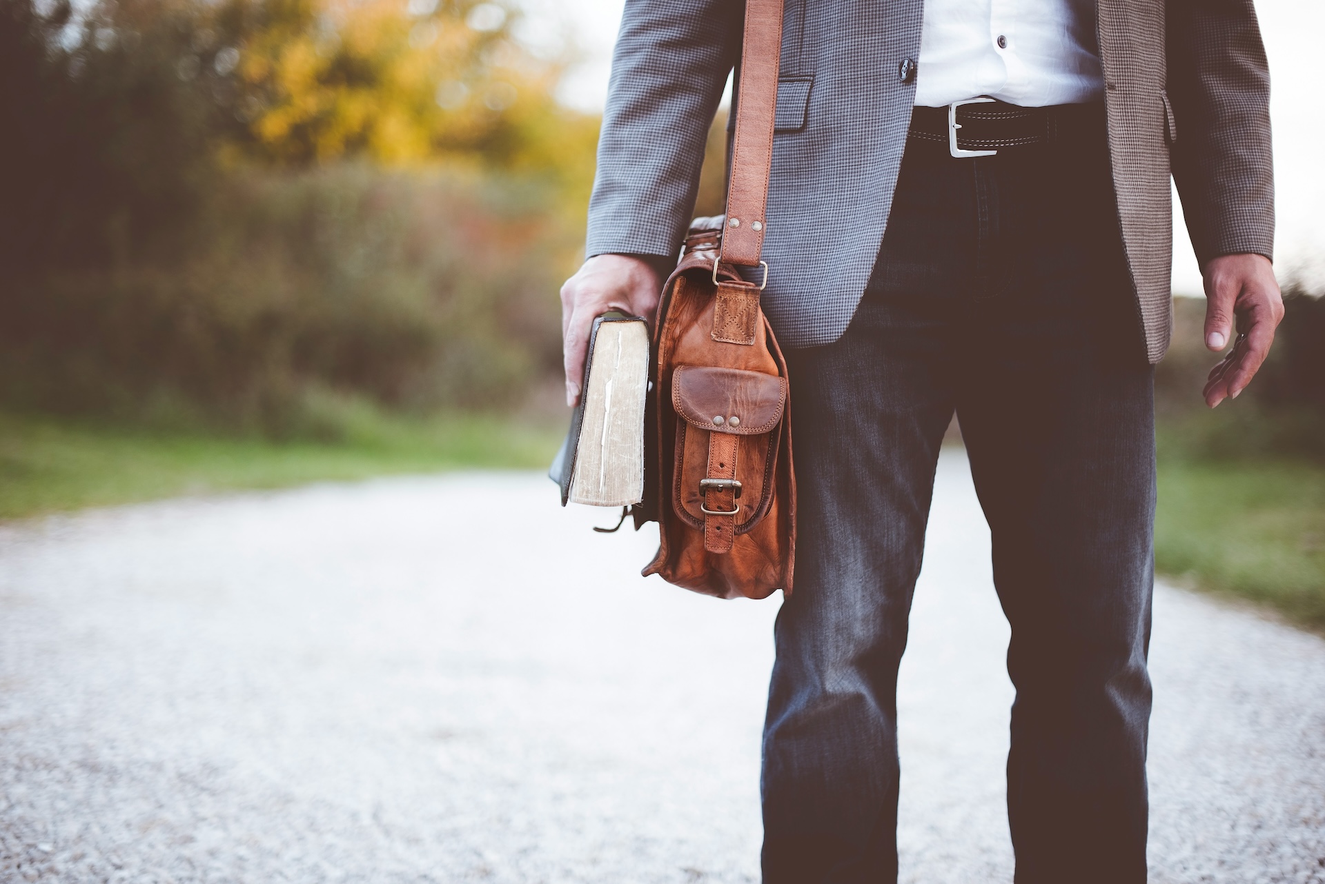 Person standing outside holding a book with a brown bag over their shoulder.