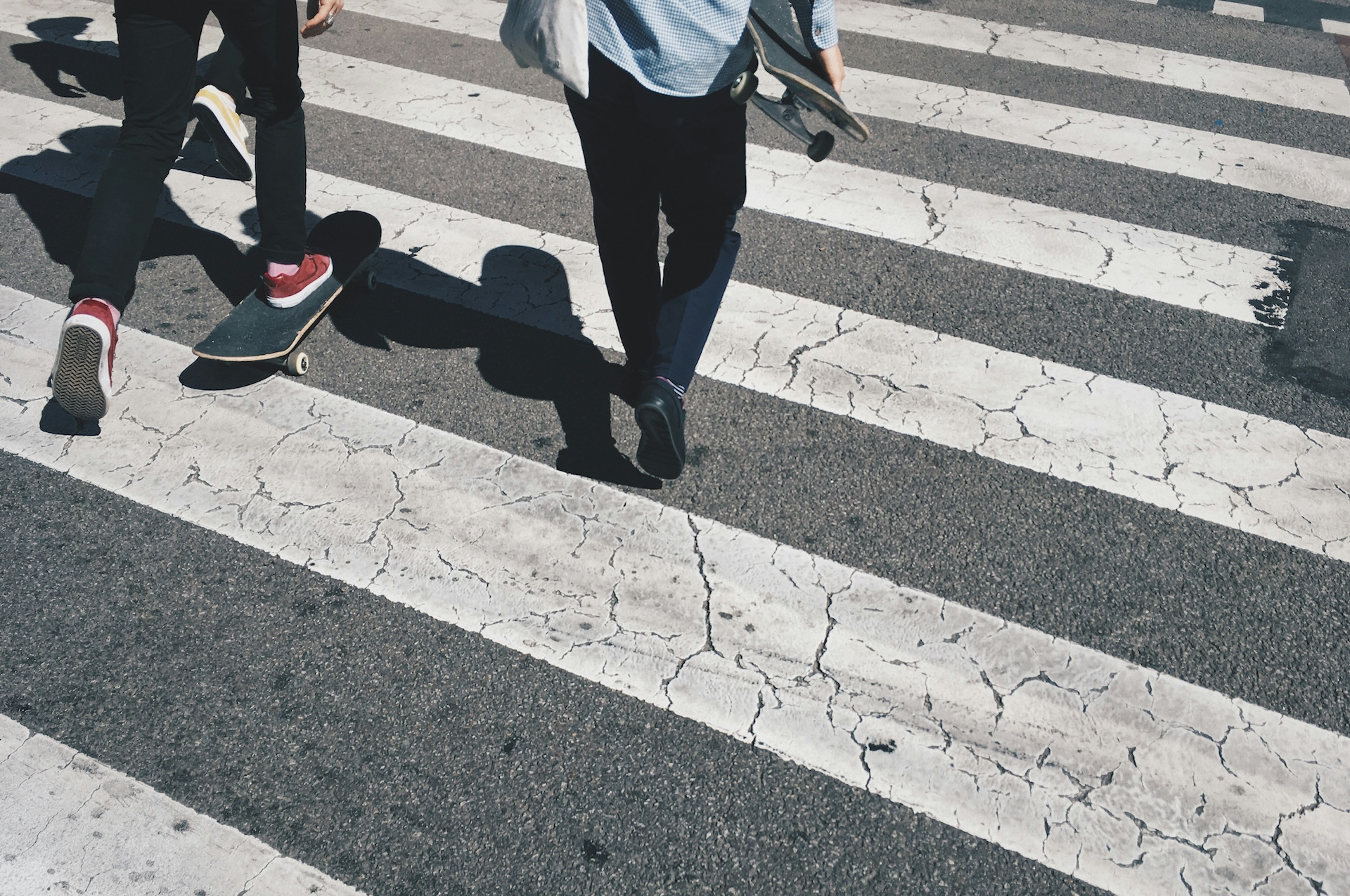 Two people walking across a road crossing. The lower half of their bodies are shown with emphasis on the road crossing pattern on the road.