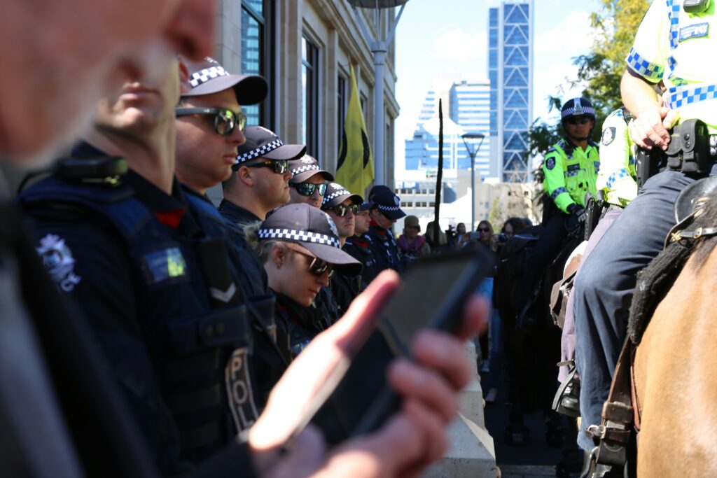 Australian Police officers standing in line while other officers are in front of them riding horses